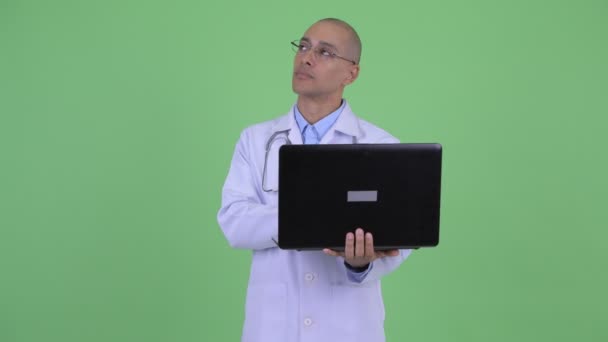 Happy bald multi ethnic man doctor thinking while using laptop — Stock Video