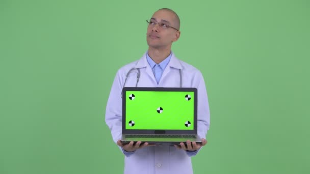 Счастливый лысый многонациональный врач думает, показывая ноутбук — стоковое видео