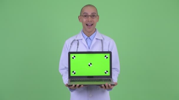 Feliz careca multi étnico homem médico mostrando laptop e olhando surpreso — Vídeo de Stock