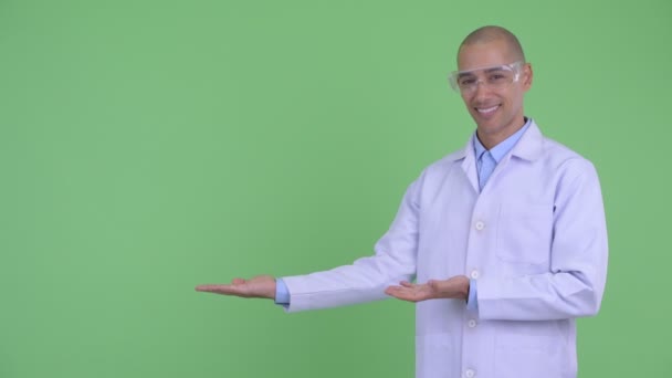 Feliz careca multi médico homem étnico com óculos de proteção mostrando algo — Vídeo de Stock