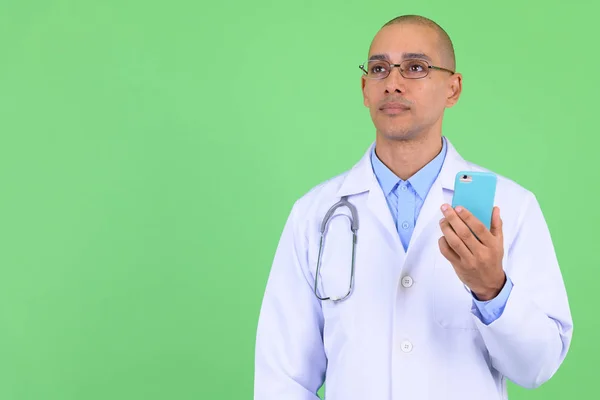 Przystojny łysy Multi etniczne człowiek lekarz myślenia podczas korzystania z telefonu — Zdjęcie stockowe