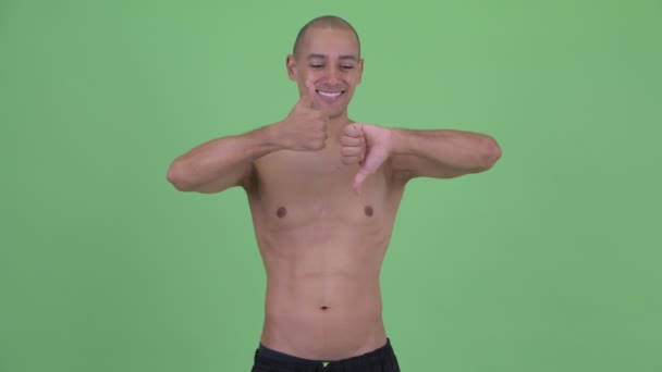 Запутавшийся лысый многонациональный мужчина без рубашки выбирает между большим и большим пальцами вниз — стоковое видео