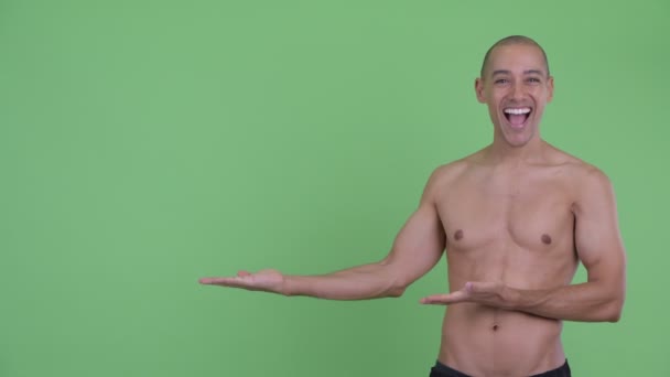 Счастливый лысый многонациональный мужчина без рубашки показывает что-то и выглядит удивленным — стоковое видео