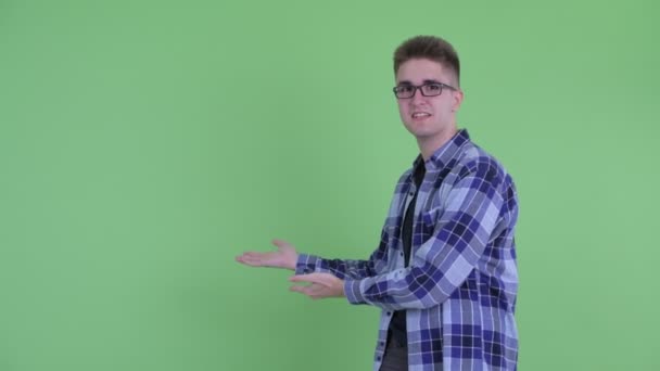 Feliz jovem hipster homem falando enquanto mostrando para trás — Vídeo de Stock