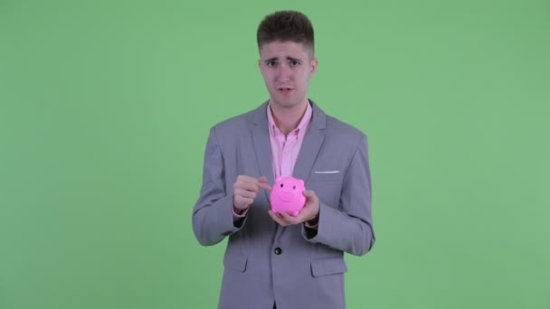 Счастливый молодой бизнесмен держит копилку и показывает большие пальцы — стоковое видео