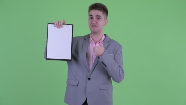 Happy young businessman showing clipboard and giving thumbs up — Stock Video