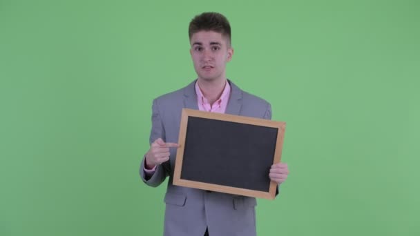 Χαρούμενος νεαρός επιχειρηματίας κρατώντας μαυροπίνακα και δίνοντας τους αντίχειρες — Αρχείο Βίντεο
