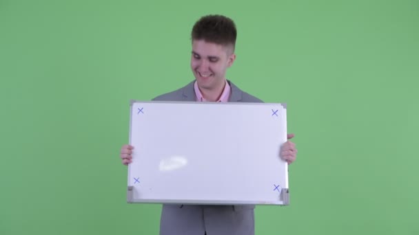 Happy young businessman holding white board and looking surprised — Stock Video