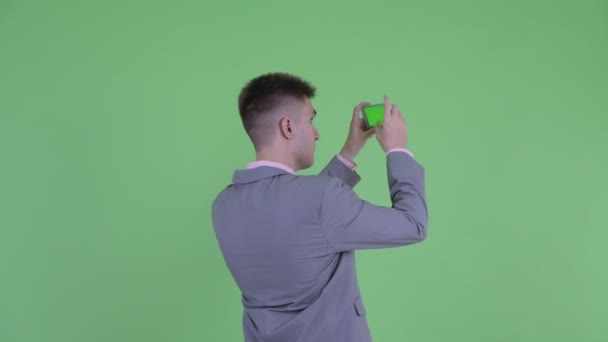 Вид спереду молодого бізнесмена, який фотографує з телефоном — стокове відео
