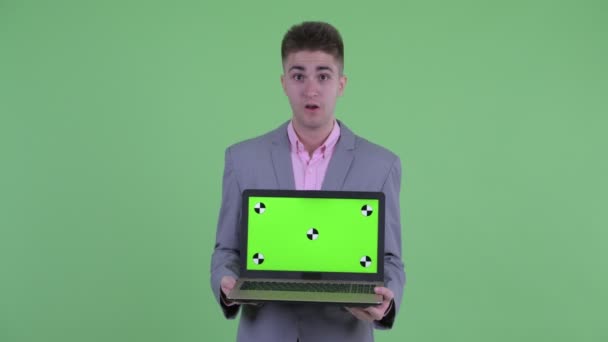 Gelukkige jonge zakenman toont laptop en op zoek verrast — Stockvideo