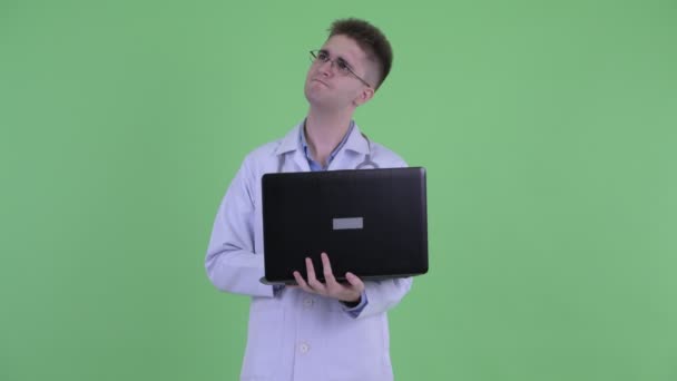 Glücklich junger Mann Arzt denken, während mit Laptop — Stockvideo