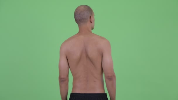 Rear view of bald multi ethnic shirtless man thinking and looking around — Stock Video