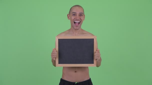 Happy bald multi ethnic shirtless man holding blackboard and looking surprised — Stock Video