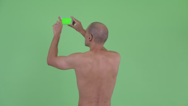 Вид сзади на лысого мужчину без рубашки, фотографирующегося с телефоном — стоковое видео
