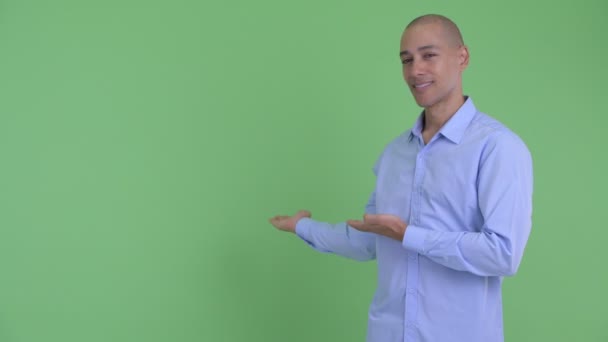 Щасливий лисий багатонаціональний бізнесмен розмовляє, показуючи назад — стокове відео