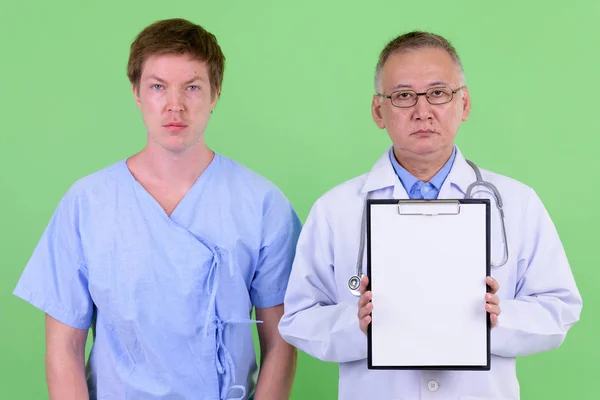 Зрелый японский врач с пациентом из Скандинавии, показывающим планшет вместе — стоковое фото