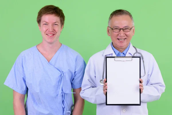 Счастливый взрослый японский врач со скандинавским пациентом, показывающим планшет вместе — стоковое фото