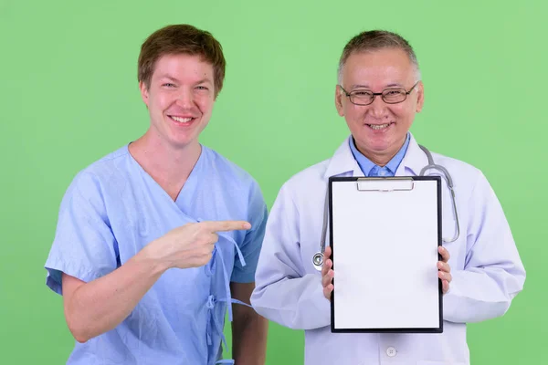 Szczęśliwy dojrzały japoński człowiek lekarz z skandynawski człowiek pacjent pokazując schowek razem — Zdjęcie stockowe