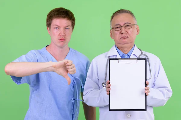 Взрослый японский врач со скандинавским пациентом, показывающий планшет и показывающий большие пальцы — стоковое фото