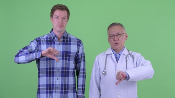 Sérieux mature japonais homme médecin avec jeune homme donnant pouces vers le bas ensemble — Video