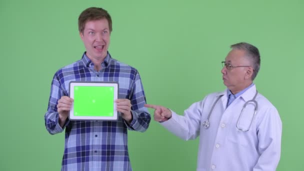 Choqué mature Japonais homme médecin avec fou jeune homme montrant tablette numérique ensemble — Video