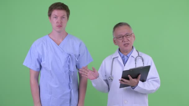 Зрелый японский врач с молодым человеком пациент объясняя что-то — стоковое видео