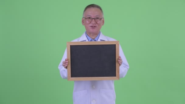 Happy mature Japanese man doctor talking while holding blackboard — Stock Video