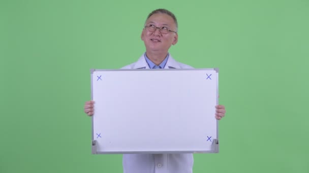 Счастливый зрелый японский врач думает, держа белую доску — стоковое видео