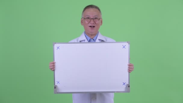 Feliz madura japonesa hombre médico hablando mientras sostiene la pizarra blanca — Vídeos de Stock