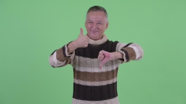 Happy confused mature Japanese man choosing between thumbs up and thumbs down — Stock Video