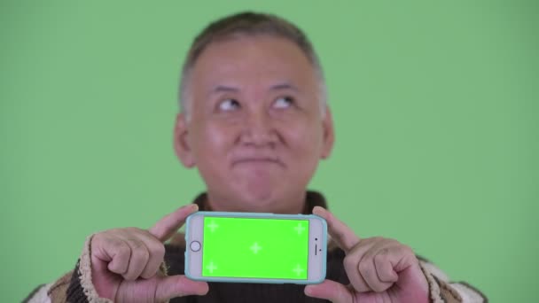 Πρόσωπο του ευτυχισμένο ώριμο ιαπωνικό άνθρωπος σκέψης, ενώ δείχνει το τηλέφωνο — Αρχείο Βίντεο