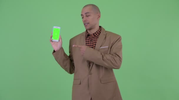 Serieuze kale multi-etnische zakenman die telefoon toont en duimen naar beneden geeft — Stockvideo