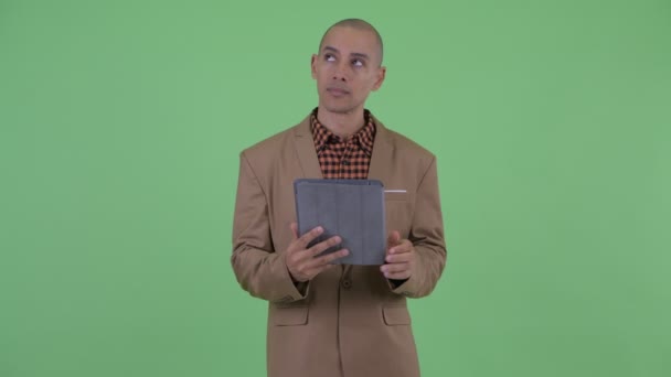 Серьезный лысый многонациональный бизнесмен думает при использовании цифрового планшета — стоковое видео