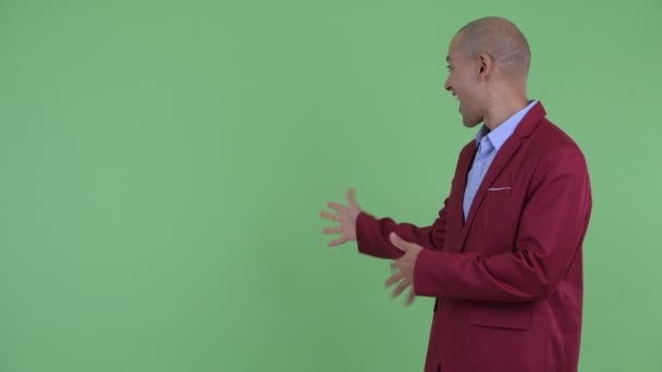 Щасливий лисий багатонаціональний бізнесмен, що показує назад і виглядає схвильованим — стокове відео