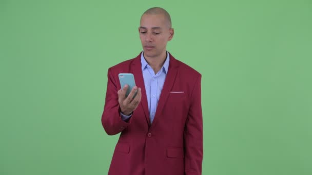 Счастливый лысый многонациональный бизнесмен с помощью телефона и выглядит удивленным — стоковое видео