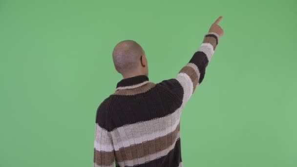 Задний вид лысого многоэтничного мужчины, указывающего пальцем, готового к зиме — стоковое видео