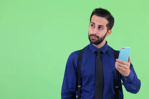 Молодой бородатый персидский бизнесмен думает, пользуясь телефоном — стоковое фото