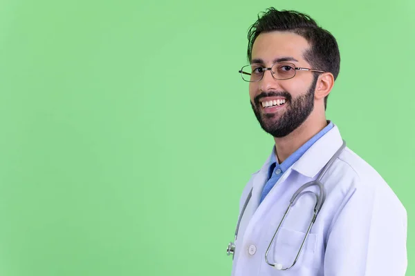 Zbliżenie widok profilu szczęśliwego młodego Brodaty Perski mężczyzna lekarz patrząc na kamerę — Zdjęcie stockowe