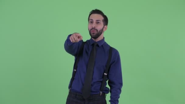 Счастливый молодой бородатый персидский бизнесмен показывает пальцем и выглядит удивлённым — стоковое видео