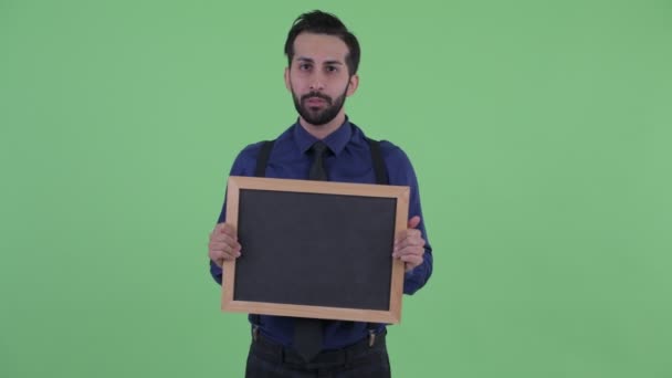 黒板を持ちながら話す幸せな若いひげペルシャのビジネスマン — ストック動画