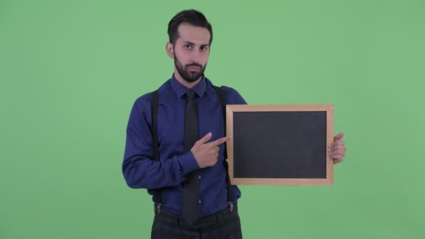 Stressed jovem barbudo persa empresário segurando quadro-negro e dando polegares para baixo — Vídeo de Stock