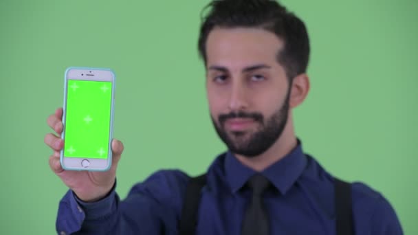 Face of happy young bearded Persian businessman showing phone — Stock Video