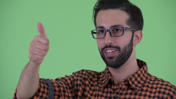 Gesicht eines glücklichen jungen bärtigen persischen Hipster-Mannes, der die Daumen senkt — Stockvideo