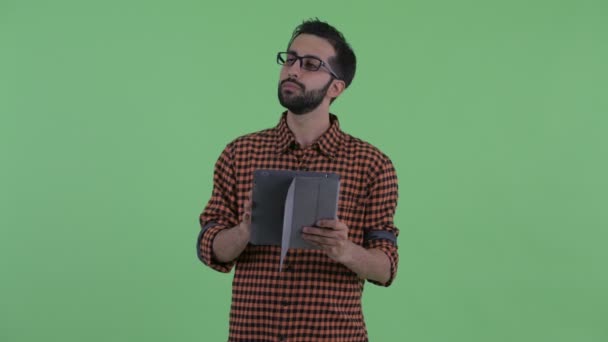 Boldog fiatal szakállas perzsa csípő ember gondolkodás használata közben a digitális tabletta — Stock videók