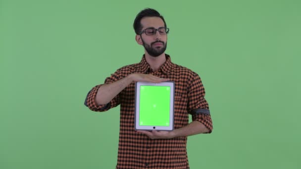 Счастливый молодой бородатый персидский хипстер думает, показывая цифровой планшет — стоковое видео