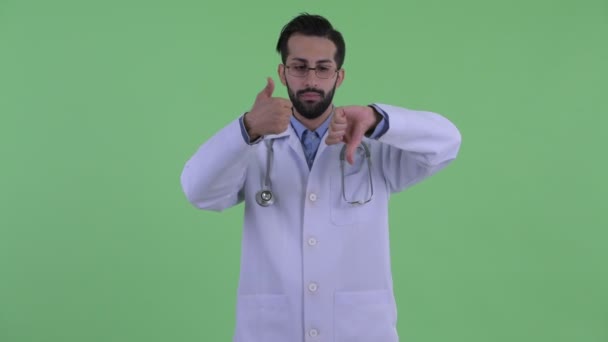 Megzavarodott fiatal szakállas perzsa férfi orvos választás között remek és remek lefelé — Stock videók