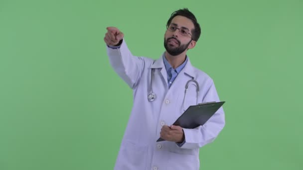 Feliz joven barbudo médico hombre persa dirigiendo mientras sostiene portapapeles — Vídeo de stock