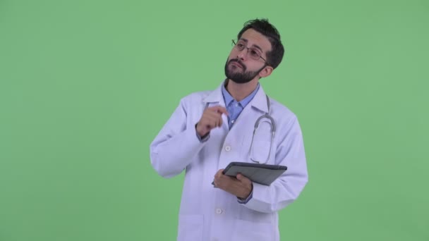 Szczęśliwy młody Brodaty Perski mężczyzna lekarz myślenia podczas korzystania z cyfrowego tabletu — Wideo stockowe