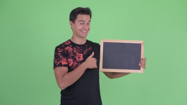 Gelukkig jonge knappe man houden blackboard en geven duimen omhoog — Stockvideo