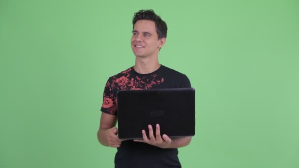 Счастливый молодой красивый мужчина думает, используя ноутбук — стоковое видео